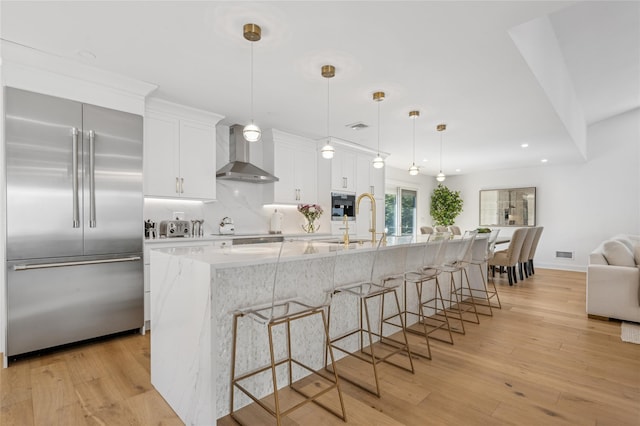 kitchen featuring light wood-type flooring, stainless steel built in fridge, tasteful backsplash, white cabinetry, and wall chimney exhaust hood