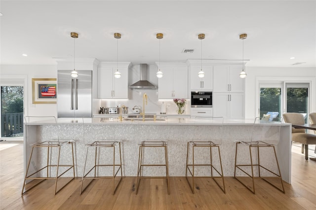 kitchen featuring visible vents, oven, wall chimney range hood, a kitchen bar, and light wood-style floors