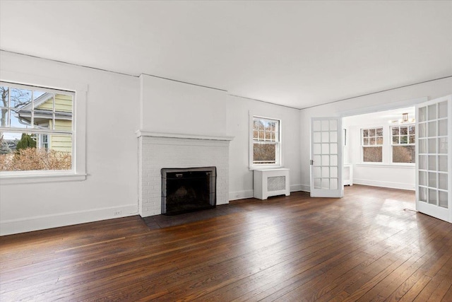 unfurnished living room with a healthy amount of sunlight, a fireplace, dark wood-type flooring, and french doors