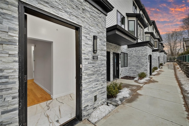 property exterior at dusk featuring stone siding, fence, and a balcony