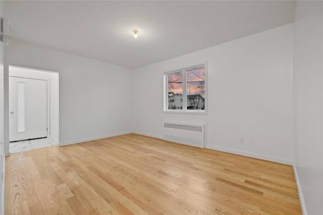 empty room with light wood finished floors, radiator heating unit, and baseboards