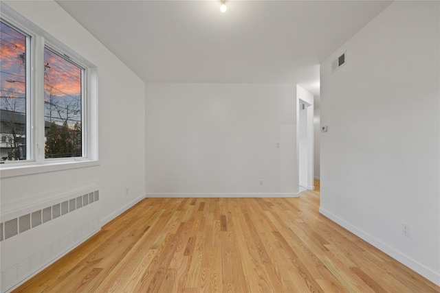 additional living space with baseboards, visible vents, light wood-style flooring, and radiator heating unit