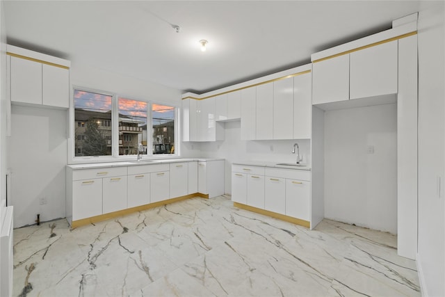 kitchen featuring marble finish floor, a sink, light countertops, and white cabinets