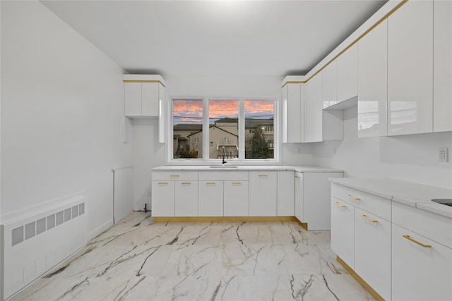 kitchen with marble finish floor, radiator, light countertops, white cabinetry, and a sink