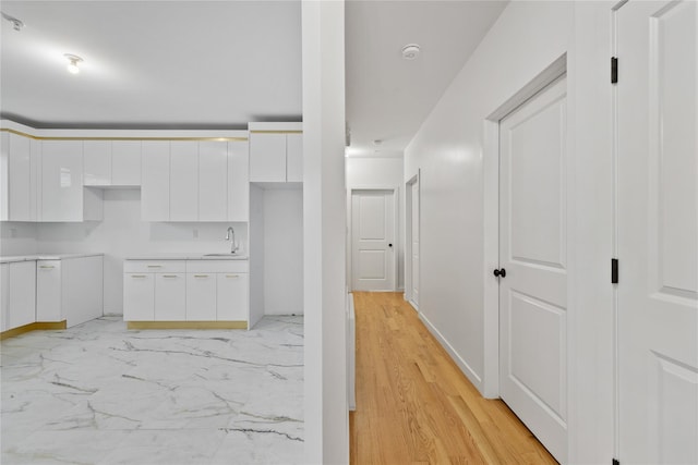 kitchen with a sink, white cabinets, marble finish floor, light countertops, and modern cabinets