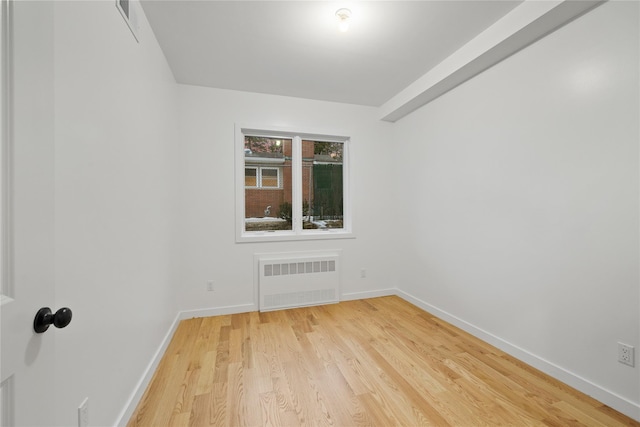 unfurnished room with baseboards, light wood finished floors, visible vents, and radiator