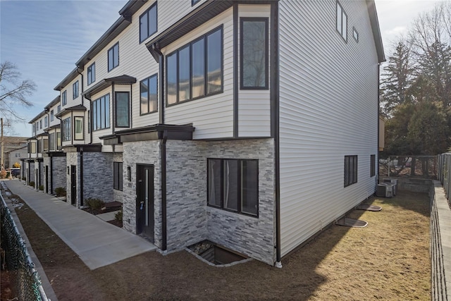 view of side of property with stone siding, central AC, and fence