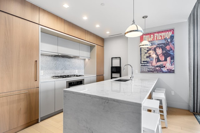 kitchen featuring light stone counters, a sink, stainless steel appliances, light wood-type flooring, and backsplash