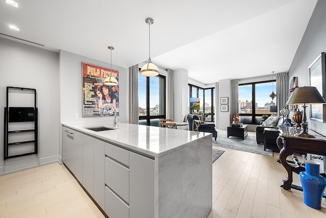 kitchen featuring light stone counters, light wood finished floors, a sink, modern cabinets, and a peninsula