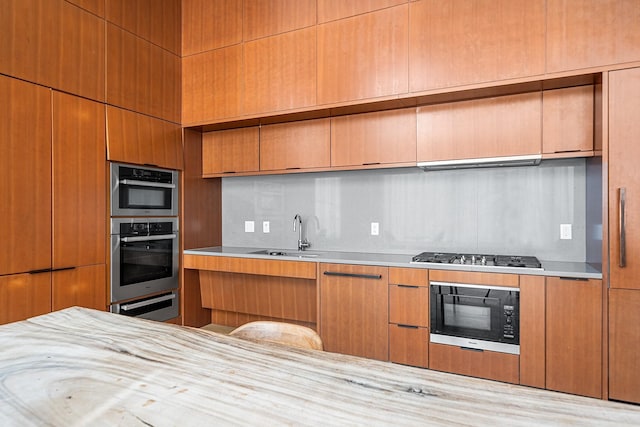 kitchen with modern cabinets, appliances with stainless steel finishes, light countertops, under cabinet range hood, and a sink