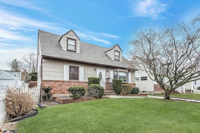 new england style home featuring brick siding, a front yard, fence, and a shingled roof