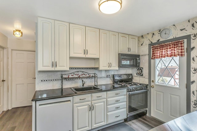 kitchen featuring black microwave, dishwashing machine, a sink, gas range oven, and dark countertops