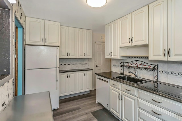 kitchen featuring white appliances, dark wood finished floors, dark countertops, a sink, and backsplash