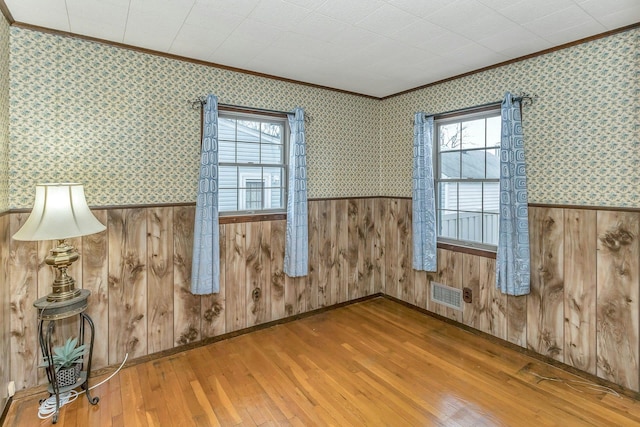 unfurnished room featuring wallpapered walls, visible vents, and a wainscoted wall