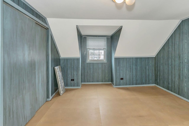 bonus room with concrete flooring, lofted ceiling, and wooden walls