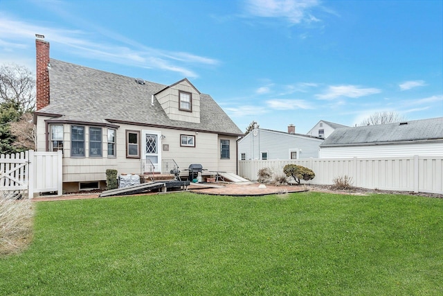 rear view of house featuring a yard, roof with shingles, a chimney, and a fenced backyard