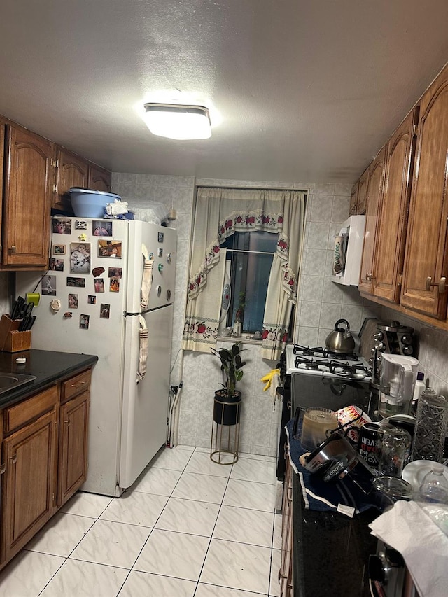 kitchen featuring brown cabinets, dark countertops, a sink, a textured ceiling, and white appliances