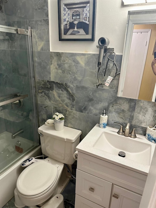 full bathroom featuring toilet, bath / shower combo with glass door, tile walls, and vanity