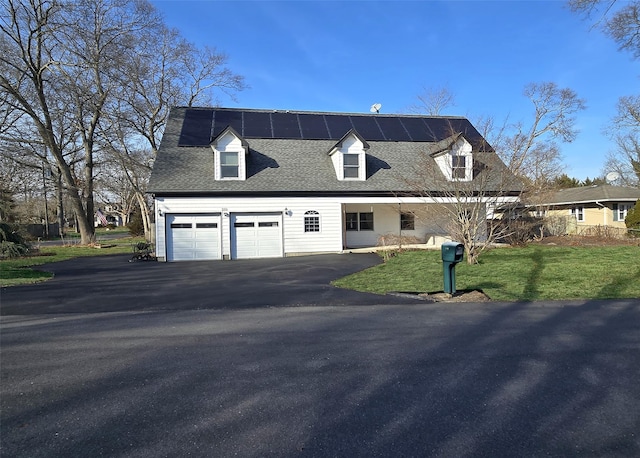 view of front facade featuring a shingled roof, a front yard, driveway, and solar panels