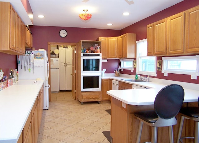 kitchen with light tile patterned floors, a peninsula, white appliances, a kitchen breakfast bar, and light countertops