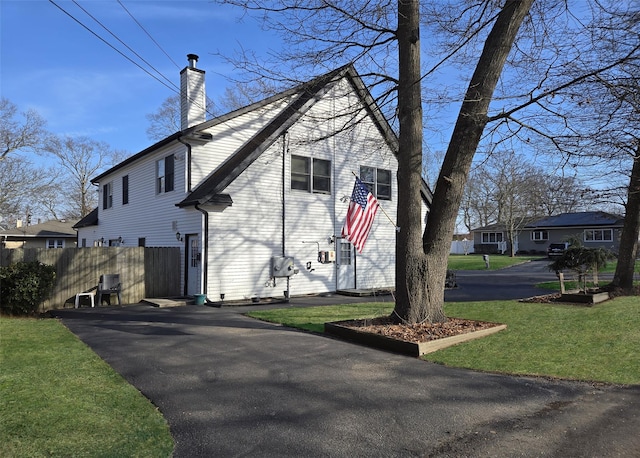 view of home's exterior featuring driveway, a chimney, fence, and a lawn