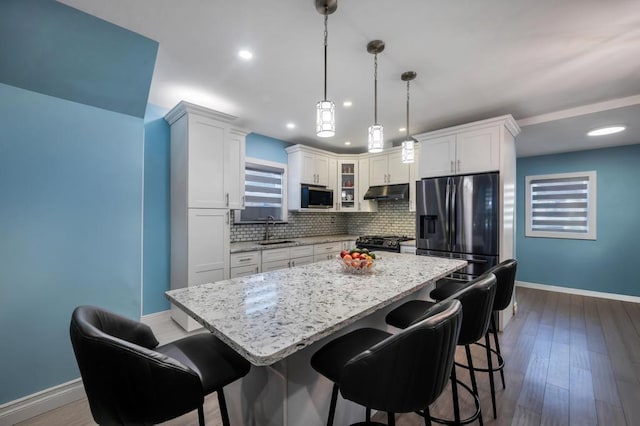 kitchen with under cabinet range hood, stainless steel appliances, a sink, white cabinets, and decorative backsplash