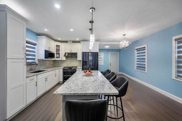 kitchen with under cabinet range hood, a breakfast bar, a sink, appliances with stainless steel finishes, and tasteful backsplash