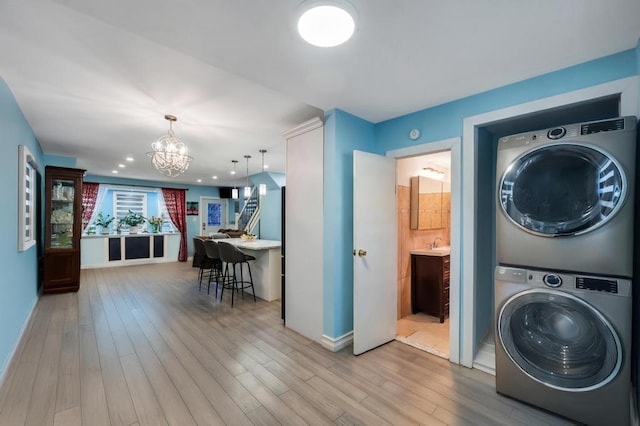 laundry room featuring light wood-type flooring, laundry area, a chandelier, and stacked washer / dryer