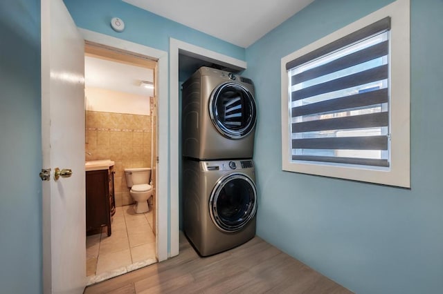 laundry room with wood finished floors, stacked washer and clothes dryer, tile walls, and laundry area