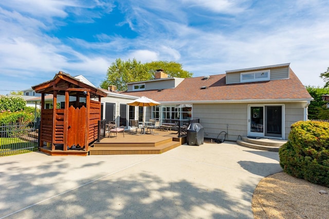 back of property with a chimney, roof with shingles, fence, a wooden deck, and a patio area