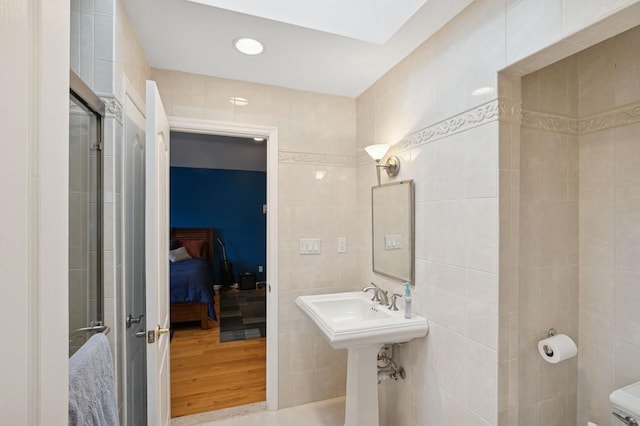 bathroom featuring a skylight, tile walls, ensuite bathroom, a sink, and wood finished floors