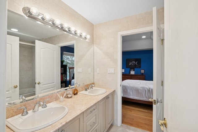 ensuite bathroom with double vanity, connected bathroom, tile walls, and a sink