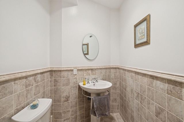 half bath with toilet, tile walls, and wainscoting