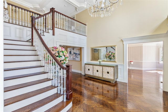 staircase with a decorative wall, a wainscoted wall, a towering ceiling, an inviting chandelier, and crown molding