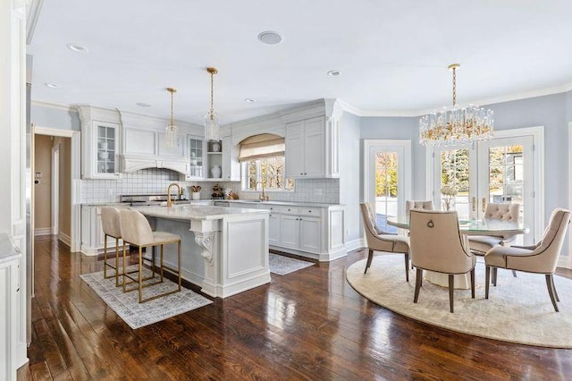 kitchen with a center island with sink, glass insert cabinets, light countertops, and dark wood-style flooring