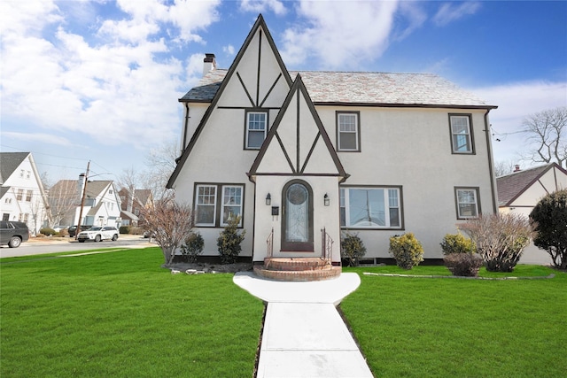 tudor home featuring a chimney, a front lawn, and stucco siding