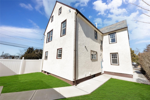 view of side of property with a yard, fence, and stucco siding