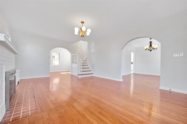 unfurnished living room featuring arched walkways, a brick fireplace, and a notable chandelier