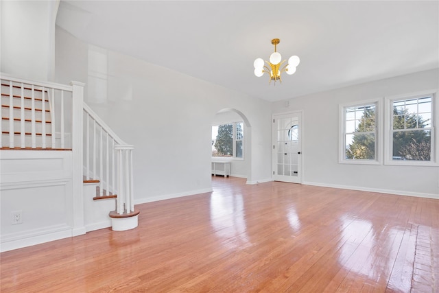 entryway with arched walkways, a notable chandelier, baseboards, stairs, and light wood finished floors