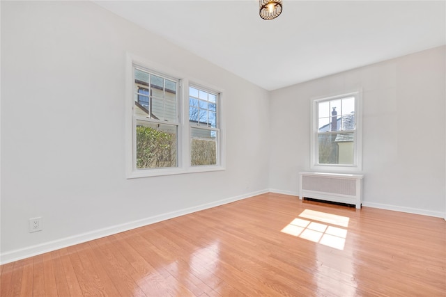 empty room featuring radiator heating unit, wood finished floors, and baseboards