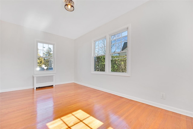 empty room with baseboards, light wood-type flooring, and radiator