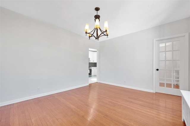 empty room featuring light wood-style flooring, baseboards, and a notable chandelier