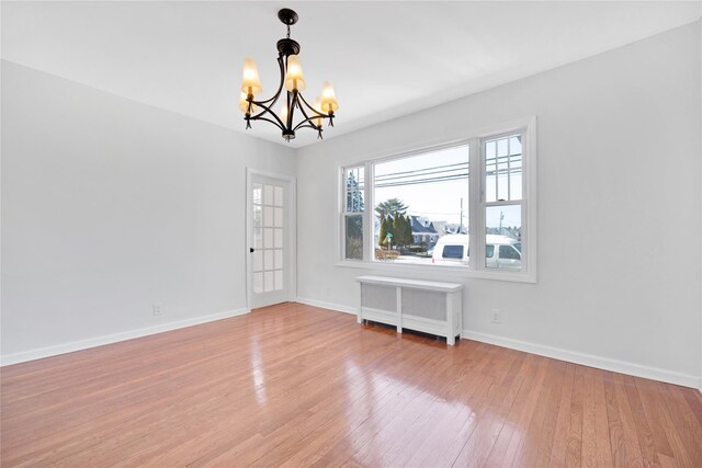 empty room with wood-type flooring, baseboards, a notable chandelier, and radiator heating unit