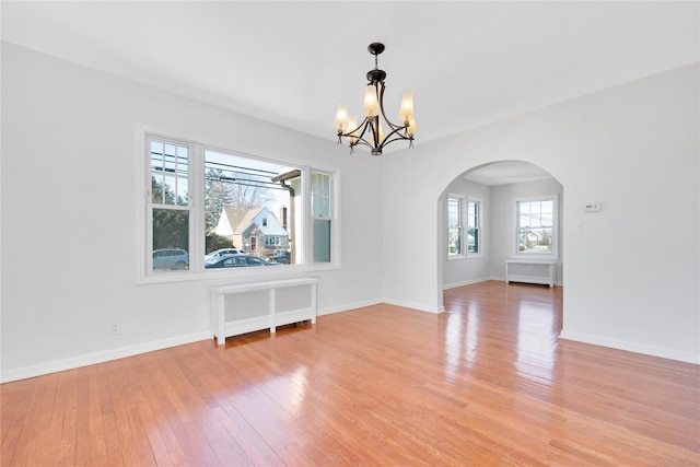 empty room with arched walkways, radiator, baseboards, and light wood finished floors