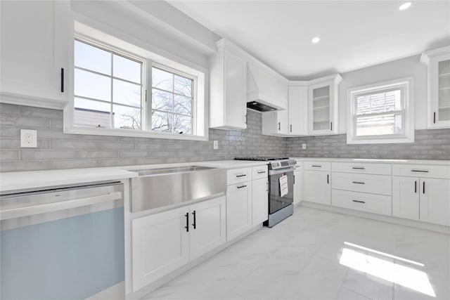 kitchen with custom exhaust hood, light countertops, appliances with stainless steel finishes, white cabinetry, and a sink