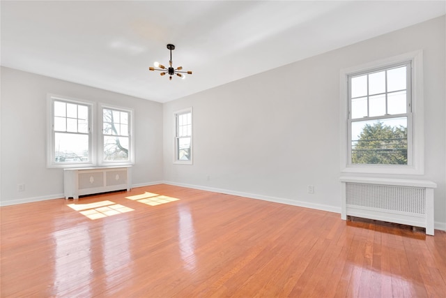 spare room with radiator, light wood finished floors, and baseboards