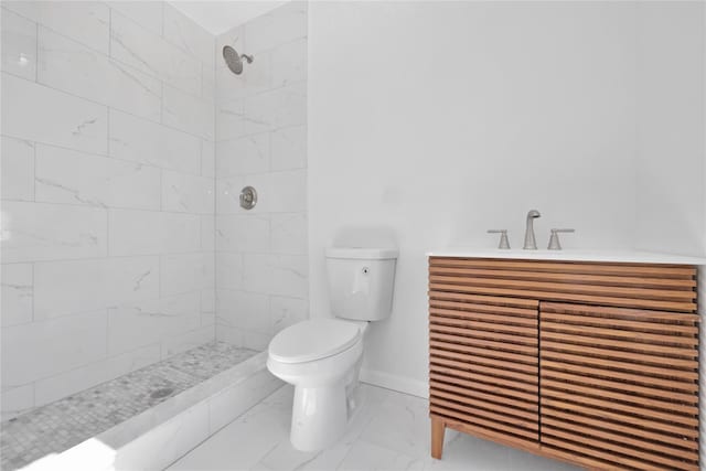 bathroom featuring marble finish floor, toilet, vanity, tiled shower, and baseboards