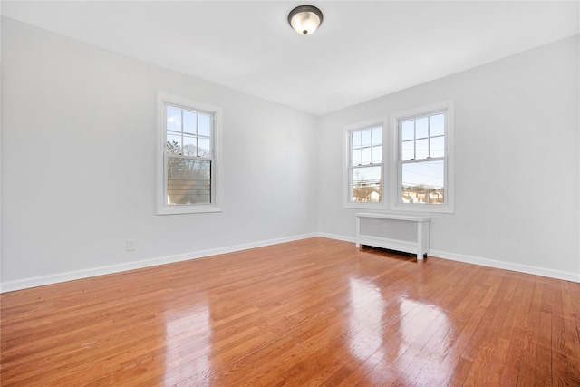 empty room featuring light wood finished floors, a healthy amount of sunlight, baseboards, and radiator