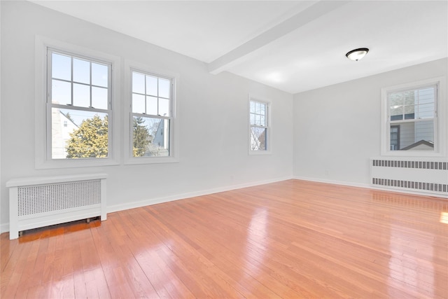 spare room with radiator heating unit, wood-type flooring, and beam ceiling