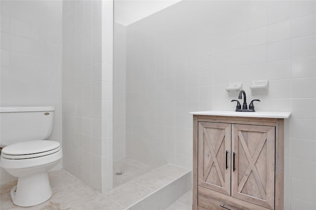 full bath featuring tile walls, toilet, a tile shower, vanity, and tile patterned flooring